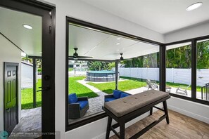 A modern patio with a bench, a hot tub, and a view of a backyard with a lawn and a fence. - Stunning 3 Bd Pool House w Enchanting Water Views (Fort Lauderdale)