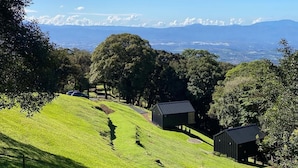 Une colline verdoyante avec deux petites cabanes et une vue dégagée sur les montagnes lointaines.