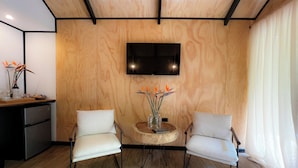 Une pièce moderne avec un mur en bois, une table ronde en bois, deux chaises blanches, un téléviseur à écran plat fixé au mur et un bureau en bois avec un ordinateur.