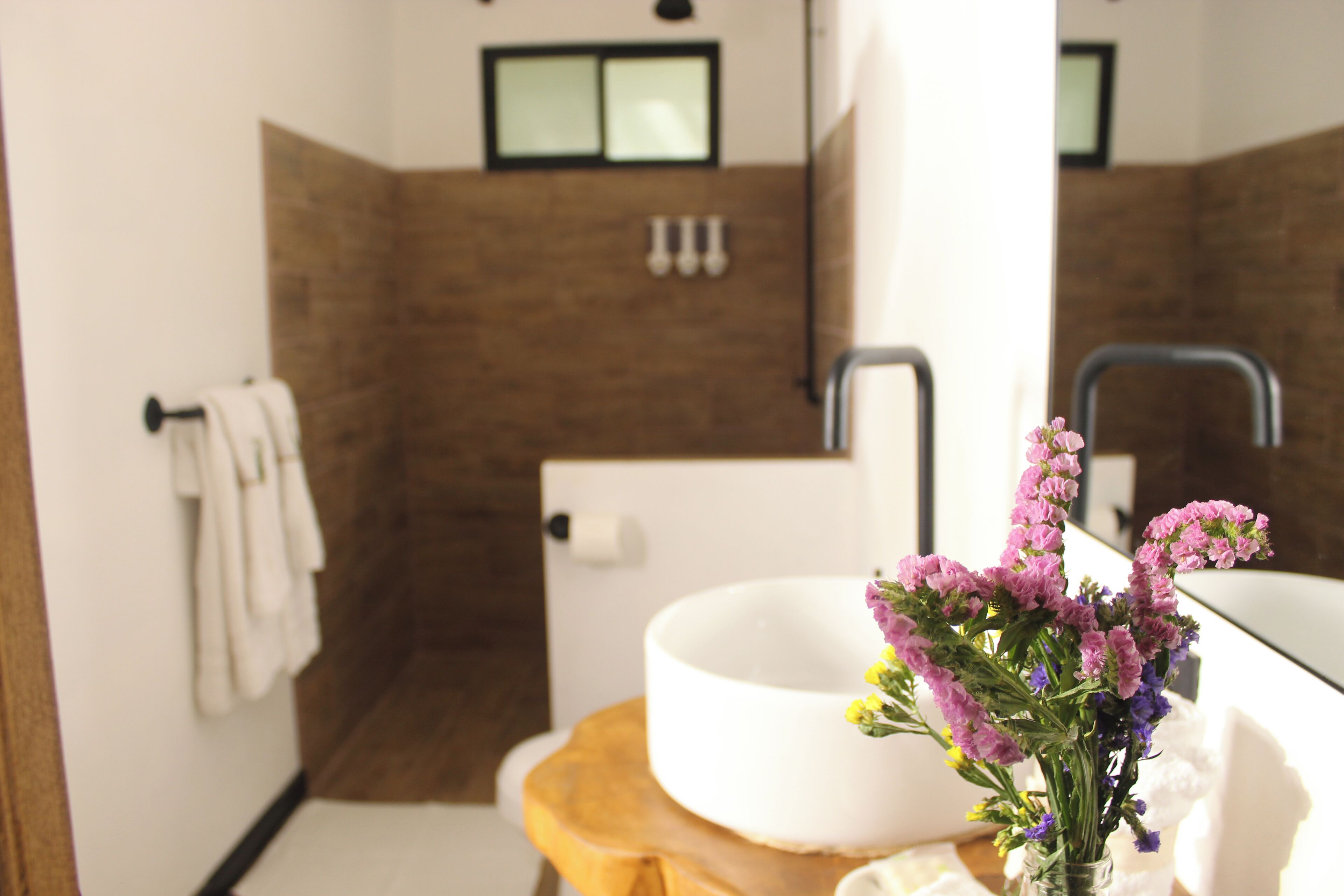 A bathroom with a white sink, a wooden stool, and a vase of purple flowers.