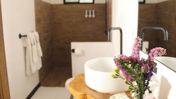 A bathroom with a white sink, a wooden stool, and a vase of purple flowers.