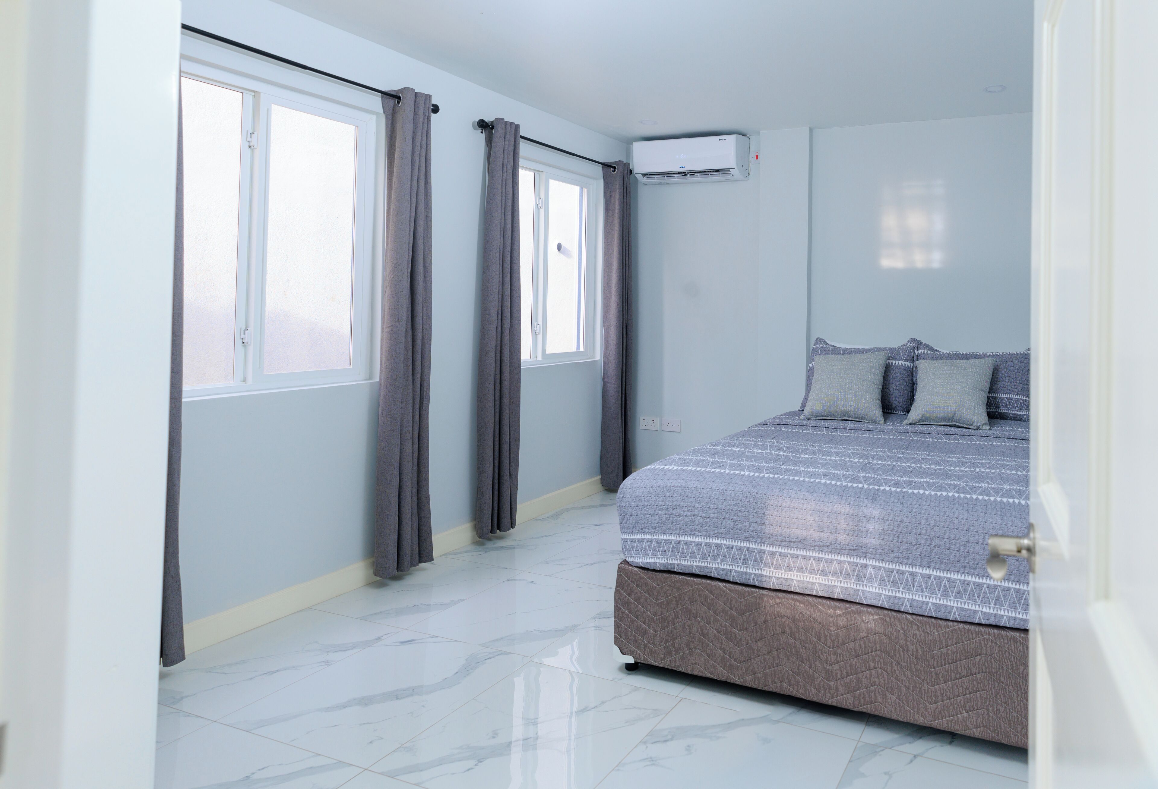 A bedroom with a bed, curtains, an air conditioning unit, and a window.