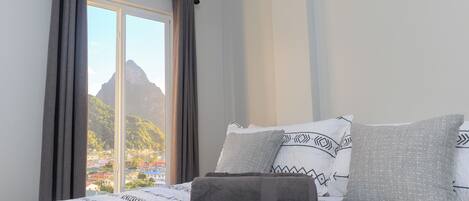 A bedroom with a bed, curtains, and a view of a mountain and buildings.