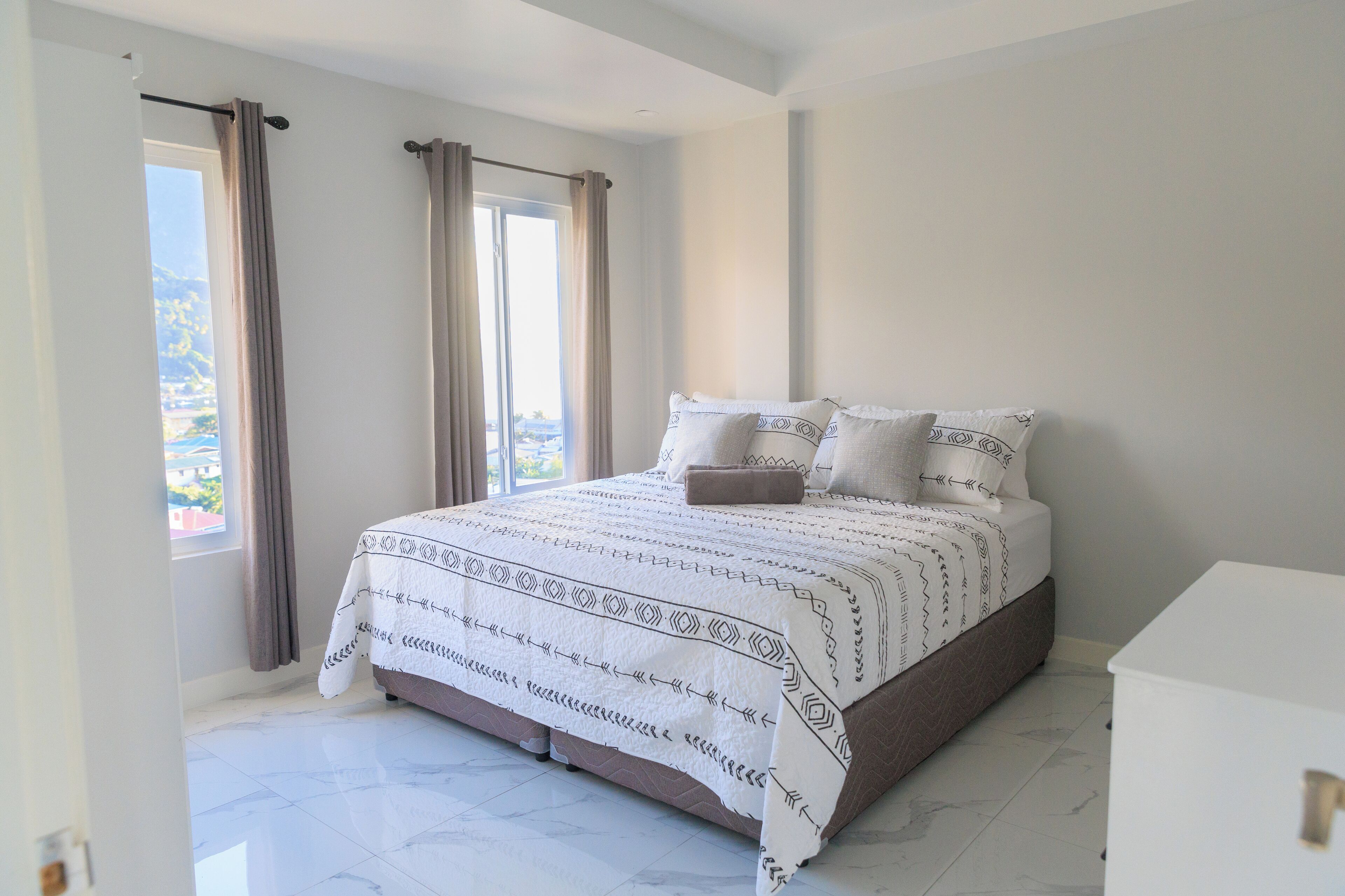 A bedroom with a bed, curtains, a window, and a white dresser.