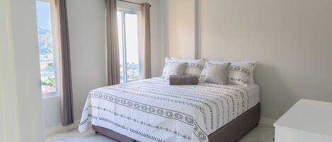 A bedroom with a bed, curtains, a window, and a white dresser.