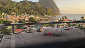 A balcony with a view of a coastal town, a mountain, and a body of water. - Caldera Villas (Soufrière)