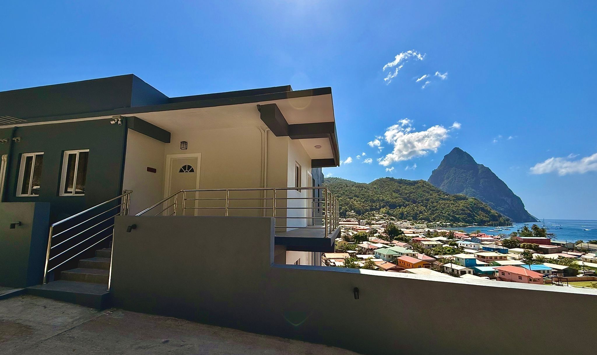 A building with a staircase leading to a balcony overlooking a coastal town and a mountain.