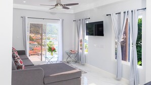 A modern living room with a sofa set, a glass table, and a ceiling fan. - Caldera Villas (Soufrière)