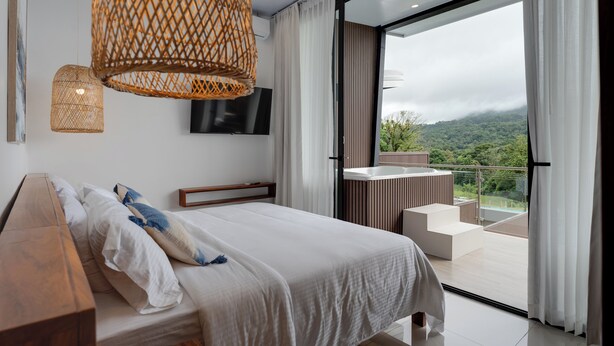 A modern bedroom with a large bed, a TV, and a balcony with a view of the mountains. - Stylish Volcano Villa w/ Jacuzzi & Private Pool, volcano views, sun deck, WiFi (La Fortuna)