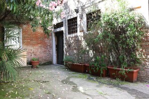 A courtyard with a brick wall, potted plants, and a door. - GuestHost - Cozy apartment of 55 sqm located on the second floor of a Venetian building without a lift (stairs to access), for 4 people.The accommodation is located in the Dorsoduro area, near the Papadopoli Gardens, Santa Lucia station and Piazzale Roma (Venezia)
