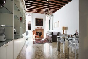 A modern kitchen with a built-in stove, a dining area with a glass table and chairs, and a living room with a sofa and fireplace.