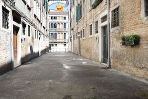 A narrow alleyway with old buildings, a balcony, and a door with a window.