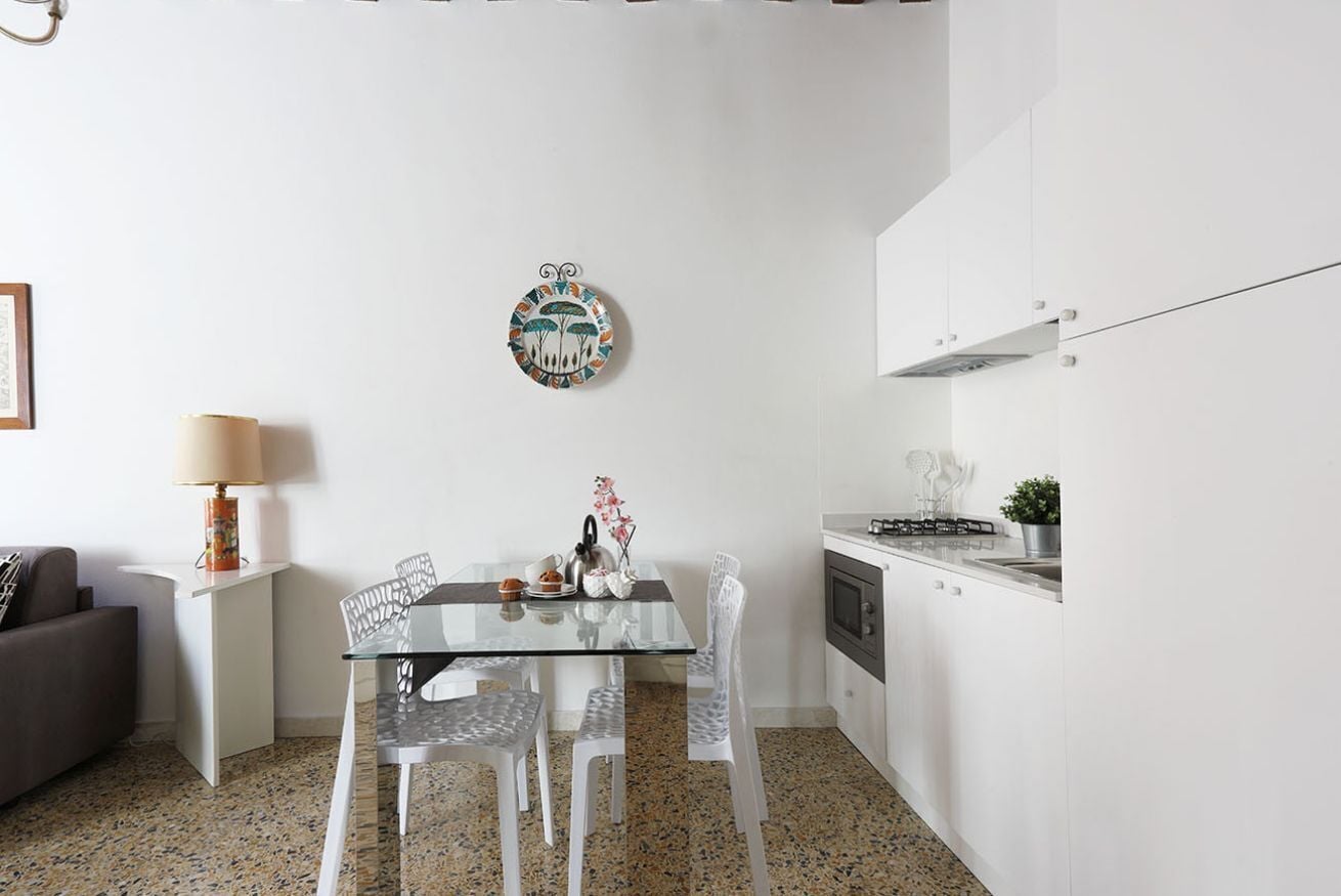 Una cocina funcional con armarios blancos, una mesa de comedor de vidrio y un adorno en la pared.