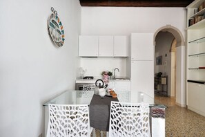 A modern kitchen with white cabinetry, a glass dining table, and a decorative wall piece.