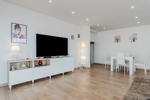 Un salon moderne doté d’un téléviseur à écran plat, de meubles blancs et d’œuvres d’art accrochées aux murs.