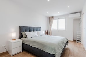 Une chambre à coucher avec un lit, une table de chevet, une lampe, une fenêtre et une armoire blanche.