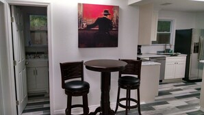 Une cuisine avec un coin repas, des meubles blancs, un réfrigérateur et un tableau accroché au mur.