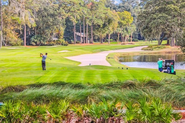 Ein Golfplatz mit Wasserschutzhindernissen, Sandbunkern und einem Clubhaus im Hintergrund.