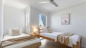 Une chambre avec deux lits, un ventilateur de plafond, une fenêtre et un tableau accroché au mur.
