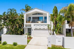 Una casa moderna de dos pisos con balcón, rodeada de plantas tropicales.