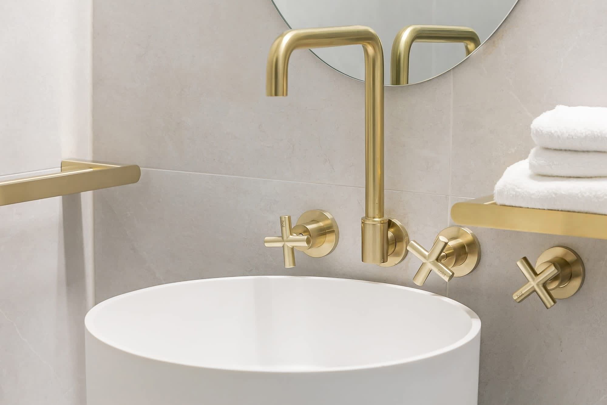 Une salle de bain avec un lavabo blanc, des robinetteries dorées et un miroir.