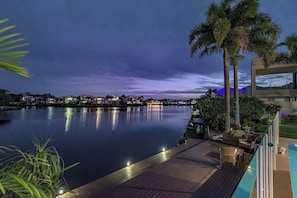 A waterfront property with a pool, palm trees, and a view of the city skyline at dusk.