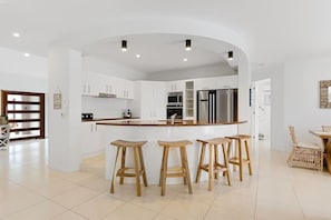 A modern kitchen with white cabinets, a stainless steel refrigerator, and wooden stools.