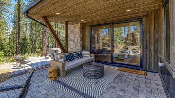 A covered outdoor seating area with a stone wall, wooden ceiling, and a bench with cushions.