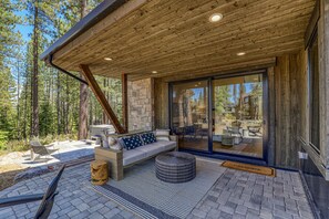 Un espacio de estar al aire libre cubierto, con pared de piedra, techo de madera y un banco con cojines.