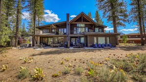 A two-story house with a large deck, surrounded by tall pine trees.