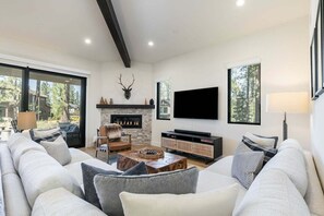 A modern living room with a fireplace, a flat-screen TV, and a large window.