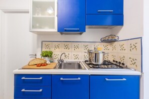 Una cocina con armarios azules, encimera blanca, pileta, estufa y un salpicadero decorativo.