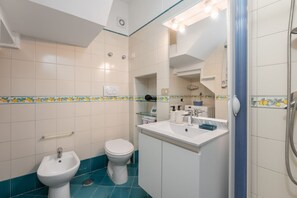 A bathroom with a white sink, a bidet, a toilet, and a shower area.