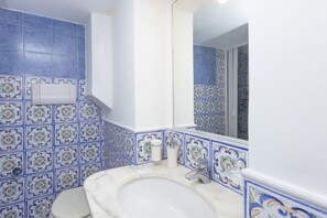 Un baño con baldosas blancas y azules estampadas, un lavamanos blanco y un espejo.