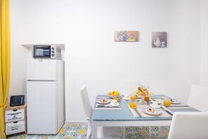 Una habitación con una mesa de comedor dispuesta para el desayuno, un refrigerador blanco y dos cuadros en la pared.