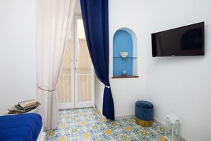 Una habitación con cama, televisión, estante pequeño, ventana con cortinas y suelo estampado.