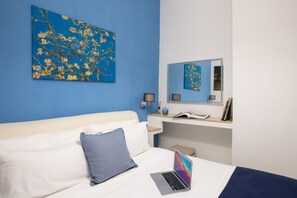 Un dormitorio con una cama, una computadora portátil, una mesita de noche, un espejo y una pared azul.