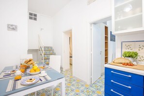 Un comedor con una mesa lista para el desayuno, una cocina con armarios azules y un suelo estampado.