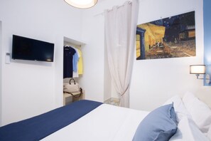 Habitació d'hotel amb un llit, una televisió, un quadre i un bany visible a través d'una porta oberta.