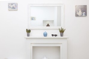 Une cheminée blanche surmontée d’un miroir, entourée de petites plantes en pot et d’un vase.