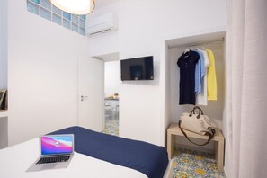 Un dormitori amb llit, ordinador portàtil, televisió, armari i bany visible a través d'una porta oberta.