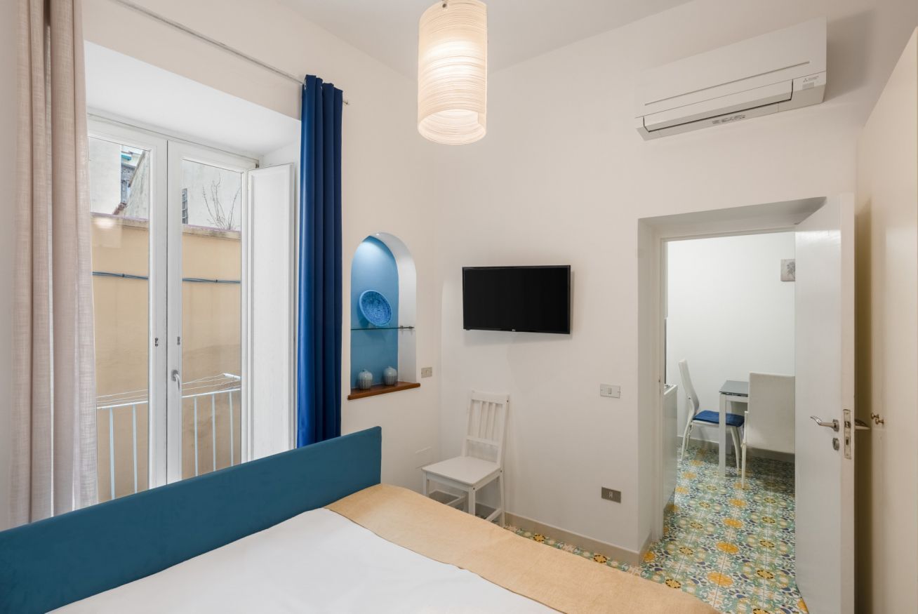 Une chambre à coucher comprenant un lit, une télévision, une chaise, un miroir et une porte donnant sur une salle de bain.