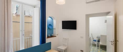 Una camera da letto con un letto, una TV, una sedia, uno specchio e una porta che dà su un bagno.