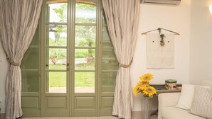A room with a green door, beige curtains, a white sofa, a vase with sunflowers, and a wall-mounted air conditioner. - Langhe Nascetta, authentic atmosphere (Novello)