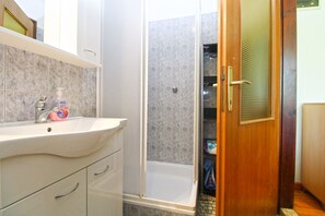 Un baño con lavamanos blanco, ducha y puerta de madera con manija de metal.