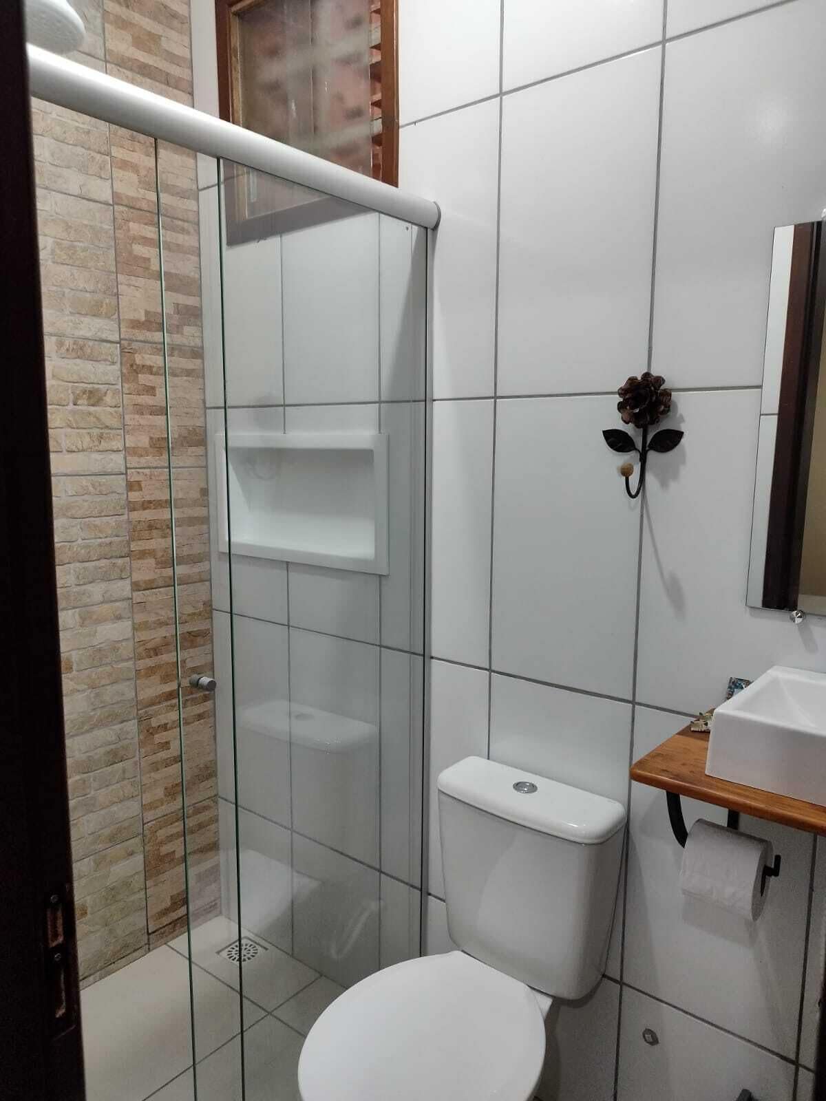 A bathroom with a glass shower enclosure, a toilet, a sink with a mirror, and a wooden shelf.