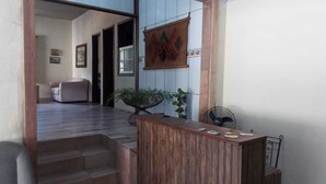 Uma área de recepção com balcão de madeira, um ventilador e uma escada que leva a outro cômodo.