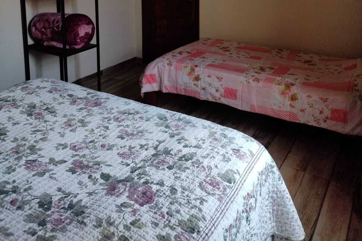 Een kleine, zwak verlichte kamer met twee eenpersoonsbedden, een donkere deur, een aan de muur bevestigde televisie en een plank met opgevouwen dekens.