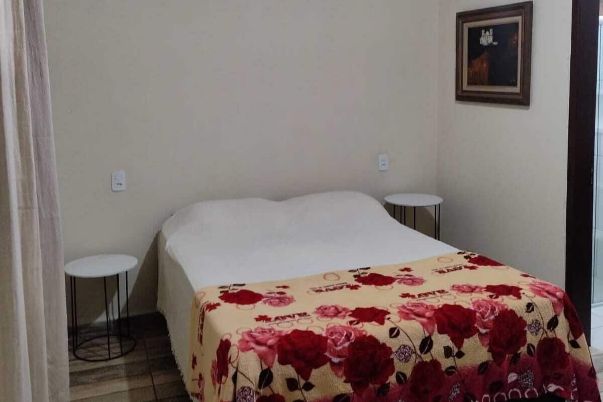 Een slaapkamer met een bed, een klein rond tafeltje en een ingelijst schilderij aan de muur.