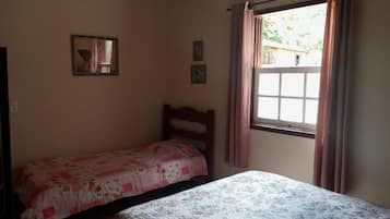 Une chambre avec deux lits simples, une fenêtre avec des rideaux et un tableau accroché au mur.